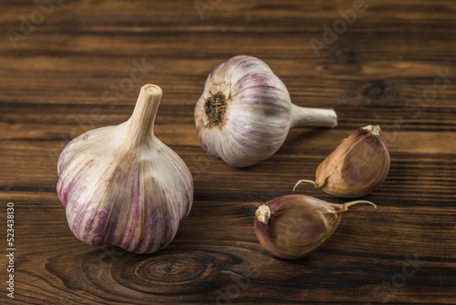 Two cloves of garlic and two heads of garlic on a wooden table.