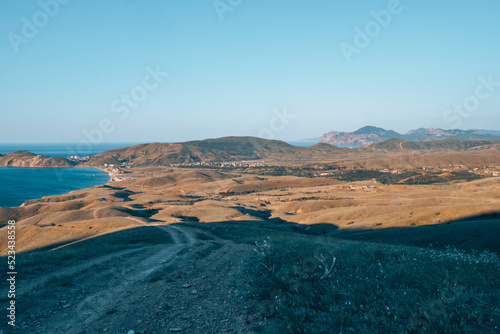 Mountainous terrain, in the distance you can see a beautiful blue ocean and blue sky. Brown hills and headlands. Travel photo style.
