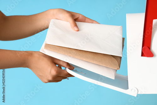 Young postwoman putting letters into mailbox on blue background, closeup