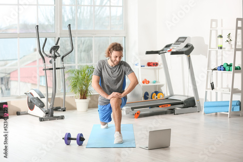 Sporty young man with laptop training in gym