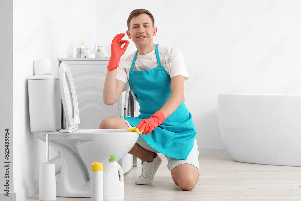 Young man cleaning toilet bowl and showing OK in bathroom Young man cleaning toilet bowl and showing OK in bathroom
