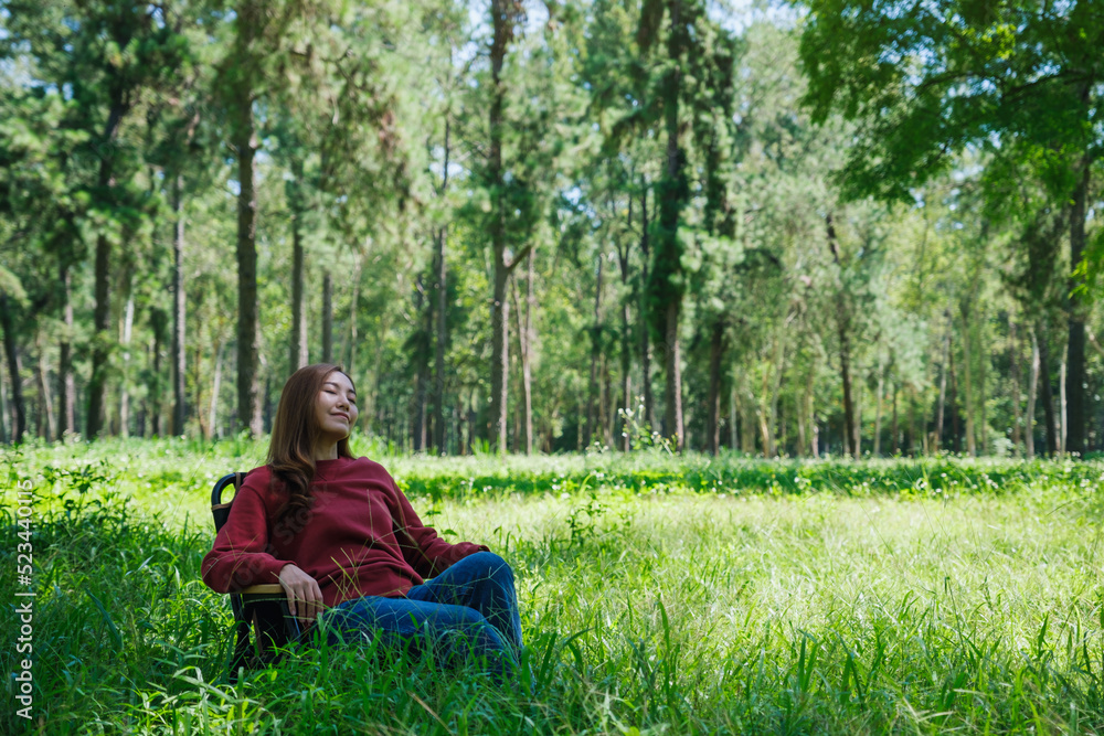 Portrait image of a beautiful young asian woman with closed eyes sitting on a chair in the park Portrait image of a beautiful young asian woman with closed eyes sitting on a chair in the park