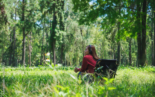 Portrait of a young woman enjoy listening to music with headphone while sitting on a camping chair in the park