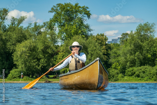 A woman of retirement age solo paddles a canoe around the Toronto Islands wearing sun safe clothing in midday sun..