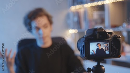 The blogger turns on the camera, speaks into it. Focus on the camera. The blogger is in the background. Curly, dark-haired guy. Vlogger, streamer. Young man. 