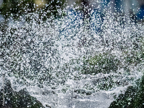 Splashes of water on dark background. Water sprays in sunny day close-up.