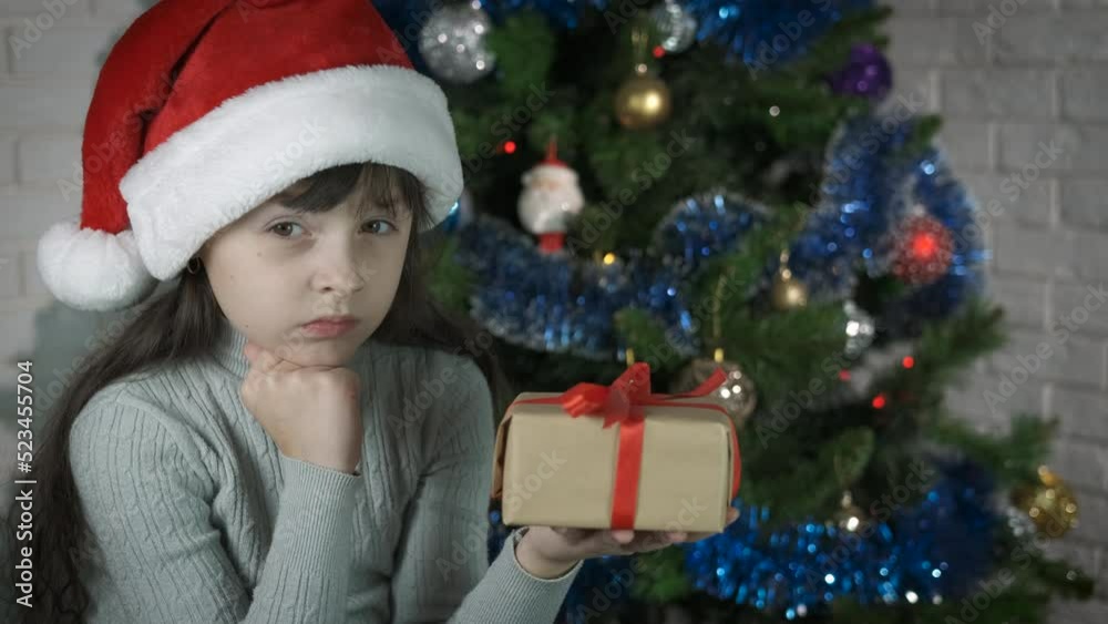 Dislike new year surprise. Offended little girl under the Christmas tree looks at her present. Dislike new year surprise. Offended little girl under the Christmas tree looks at her present.