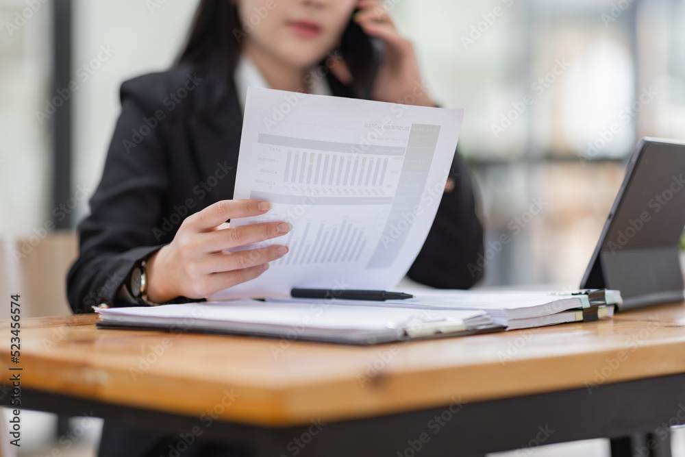 Business Asian woman talking on the phone and working with laptop calculator document on an office desk, planning analyzing the financial report, business plan investment, finance analysis concept. Business Asian woman talking on the phone and working with laptop calculator document on an office desk, planning analyzing the financial report, business plan investment, finance analysis concept.
