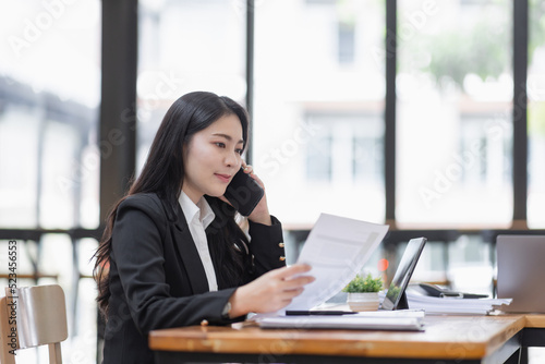 Business Asian woman talking on the phone and working with laptop calculator document on an office desk, planning analyzing the financial report, business plan investment, finance analysis concept.