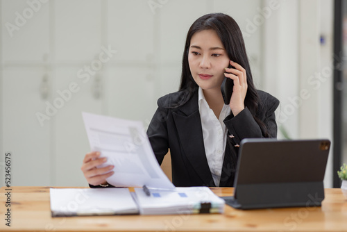 Business Asian woman talking on the phone and working with laptop calculator document on an office desk, planning analyzing the financial report, business plan investment, finance analysis concept.