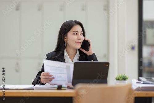 Business Asian woman talking on the phone and working with laptop calculator document on an office desk, planning analyzing the financial report, business plan investment, finance analysis concept. © David