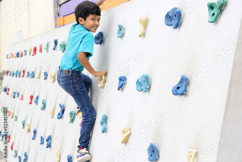 Latin dark-haired male child with blue t-shirt practicing sports wall climbing without fear of heights and exercising