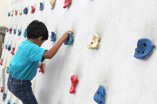 Latin dark-haired male child with blue t-shirt practicing sports wall climbing without fear of heights and exercising