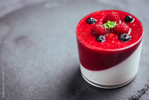 Panna cotta dessert with sauce from berries. Cherries, raspberries and blueberry as decoration. Served in two glasses on dark background. Traditional Italian creamy dessert. photo