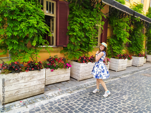 Young woman walking on the street of Lviv. Beautiful girl in white blue dress and straw hatenjoying visiting Lviv. Summer vacations.