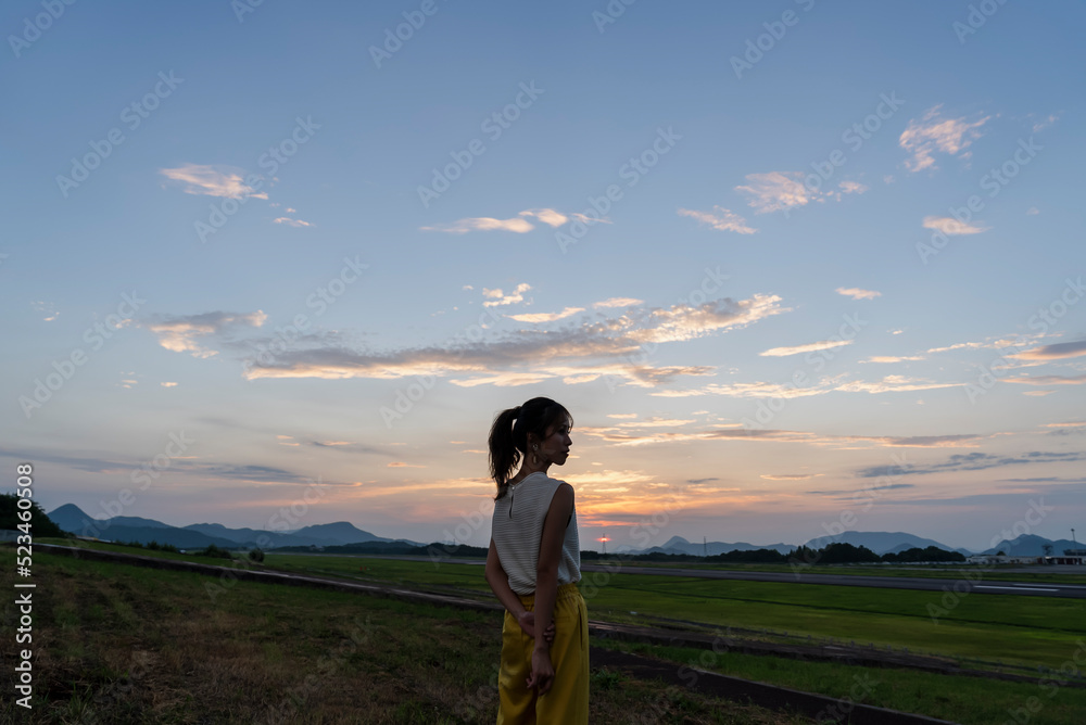 夕暮れの飛行場を眺める女性