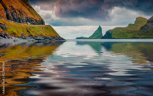 Green Tindholmur cliffs reflected in calm waters of Atlantic Ocean. Great morning view of Vagar island, Denmark, Europe. Breathtaking summer scene of Faroe Islands. Traveling concept background.. photo