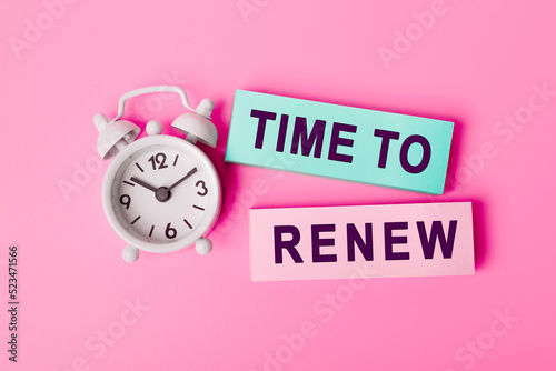 White alarm clock isolated on vivid pink background with text TIME TO RENEW, written on paper notes. Closeup of a personal agenda, top view. Motivational quote