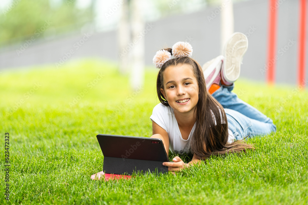 Little girl sitting on grass and playing tablet pc Little girl sitting on grass and playing tablet pc