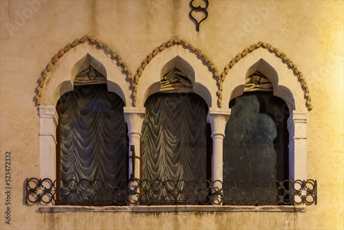 Tre finestre caratteristiche e attaccate, con balaustra in ferro e tendaggi,  in stile gotico di un antico e storico palazzo del centro cittadino. Fotografia notturna. photo