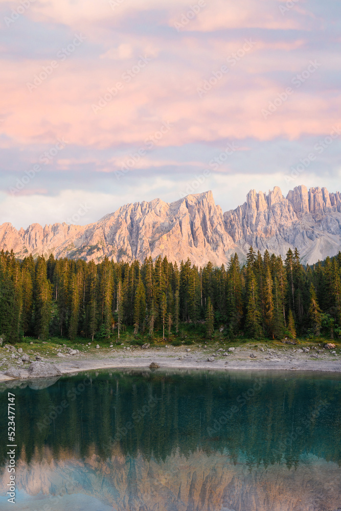 Stunning view of Carezza Lake (Lago di Carezza) with its emerald green waters, beautiful trees and mountains in the distance during a dramatic sunset
