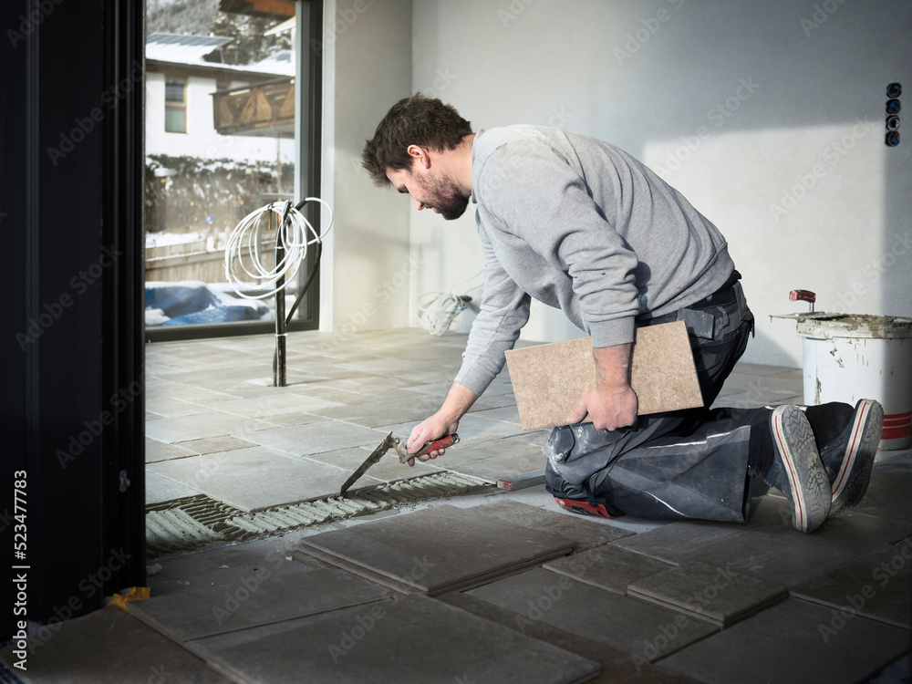 Tiler applying adhesive on floor at construction site Tiler applying adhesive on floor at construction site