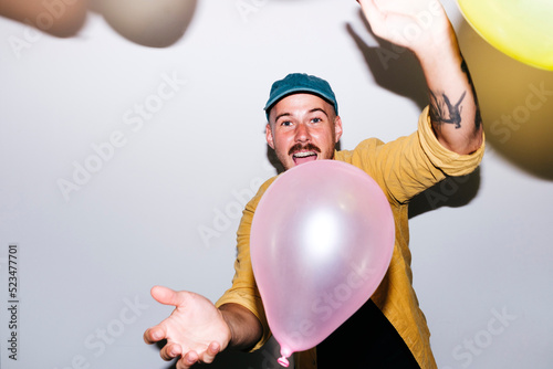 Happy man enjoying with balloons in front of wall at home photo