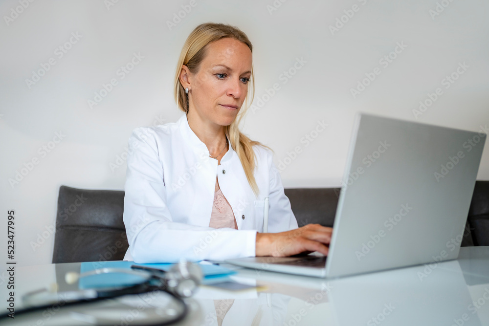 Female doctor using laptop at desk in medical practice Female doctor using laptop at desk in medical practice