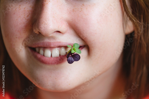 Smiling girl with fresh microgreens in mouth photo