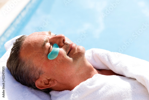 Smiling mature man with collagen patch below eye at pool spa photo