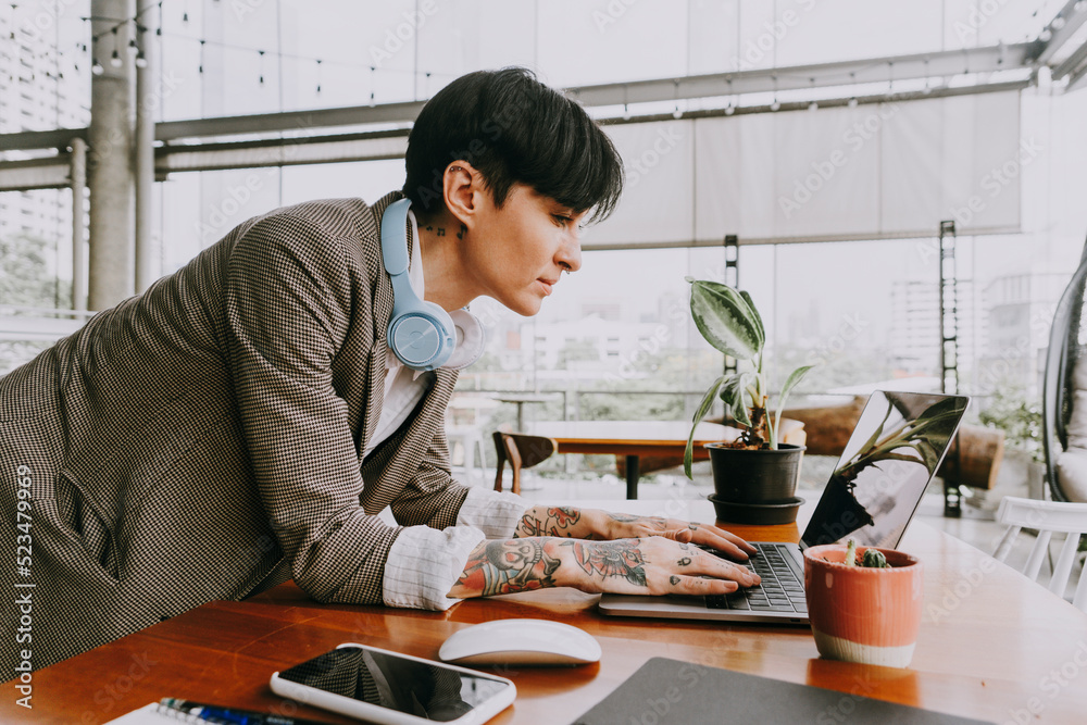 Businesswoman with short hair using laptop leaning on table Businesswoman with short hair using laptop leaning on table