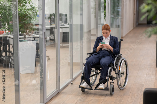 Caucasian woman using mobile phone in wheelchair at office. 