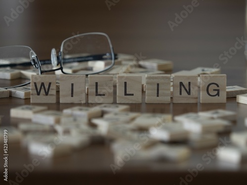 Willing word or concept represented by wooden letter tiles on a wooden table with glasses and a book photo