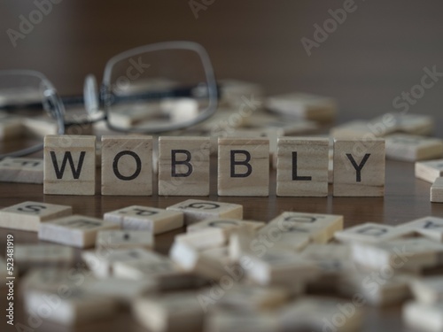 Wobbly word or concept represented by wooden letter tiles on a wooden table with glasses and a book
