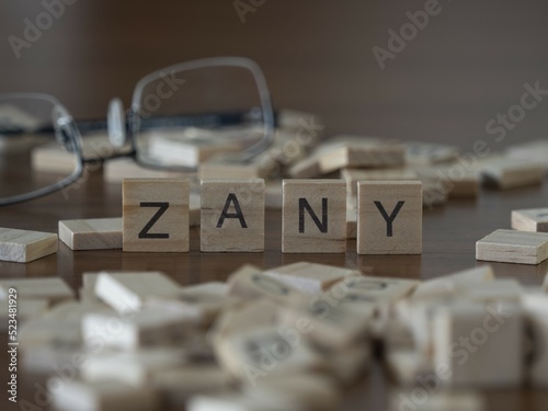 Zany word or concept represented by wooden letter tiles on a wooden table with glasses and a book photo