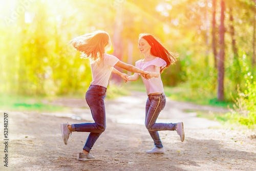 Two cheerful girlfriends are spinning holding hands, on a walk in the summer forest photo
