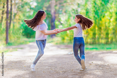 Two funny girls spinning holding hands, walking in the summer forest