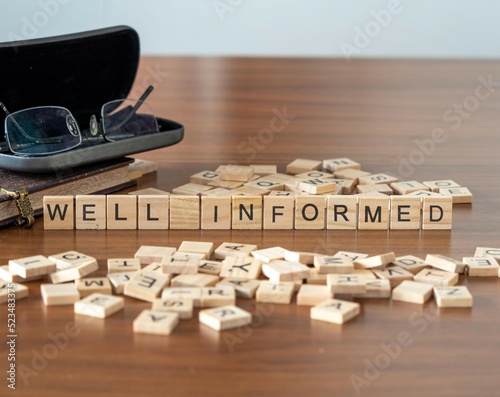 well informed word or concept represented by wooden letter tiles on a wooden table with glasses and a book