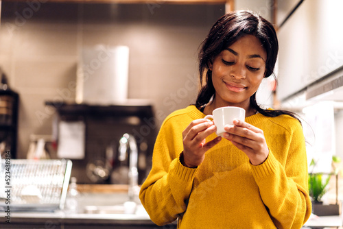 Fotografi Portrait of smiling happy african american black woman relaxing drinking and looking at cup of hot coffee or tea