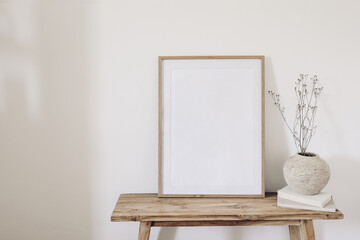 Winter, fall still life. Dry grass, plant bouquet in rustic ceramic vase. Old books on wooden bench. Blank vertical picture frame mockup. White wall background. Empty copy space. Scandinavian nterior