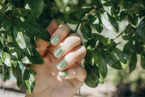 Female hand with summer nail design. Glitter green nail polish manicure. Hand with green manicure hold green leaves
