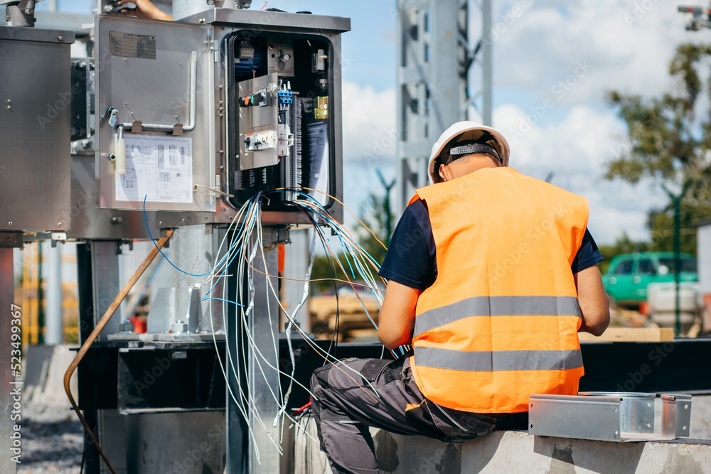 Adult electrical engineer inspect the electrical systems at the equipment control cabinet. Installation of modern electrical station Adult electrical engineer inspect the electrical systems at the equipment control cabinet. Installation of modern electrical station