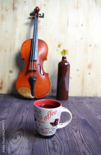 cup of coffee, violin and bottle with flowers on wooden table