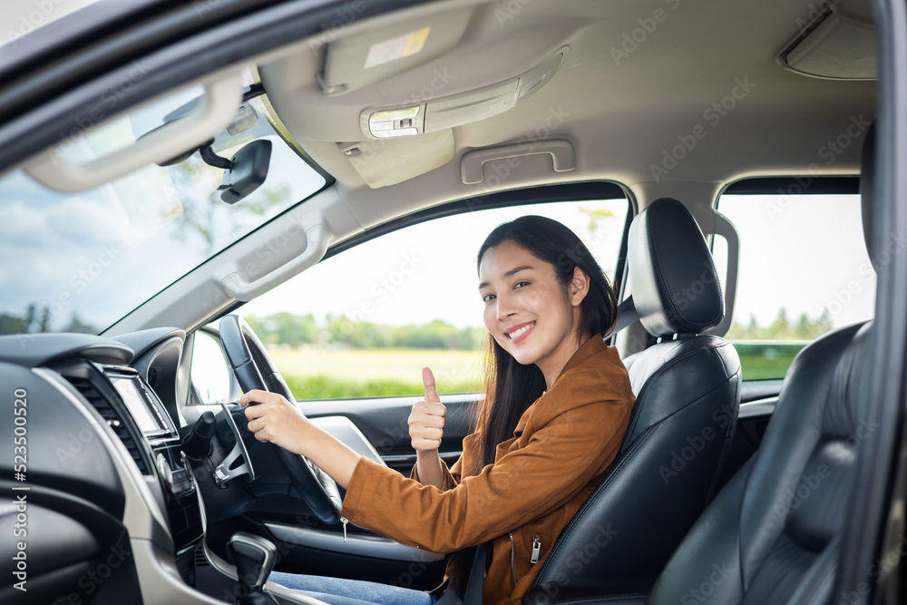 Young beautiful asian women getting new car. she very happy and excited. Smiling female driving vehicle on the road on a bright day.