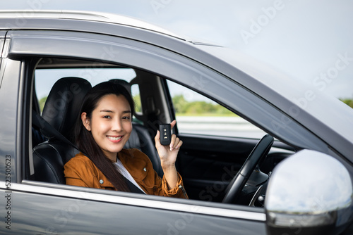 Young beautiful asian women getting new car. she very happy and excited looking outside window in hand holding car key. Smiling female driving vehicle on the road on a bright day