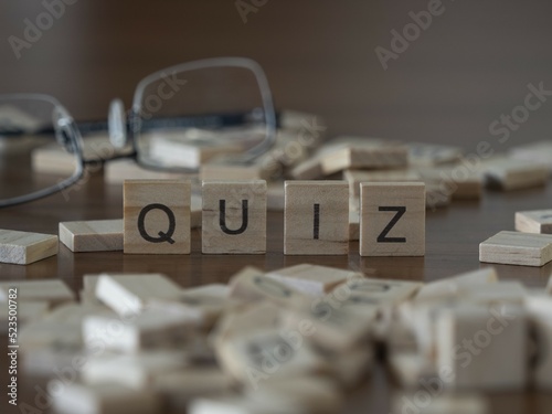 Quiz word or concept represented by wooden letter tiles on a wooden table with glasses and a book photo