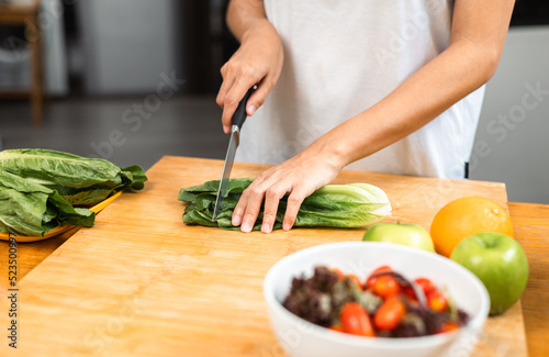 Female slicing and cooking green apple on cutting board for vegetable salad in weight loss diet. Beautiful woman happily cooks a healthy breakfast in kitchen in the morning. Diet food concept.