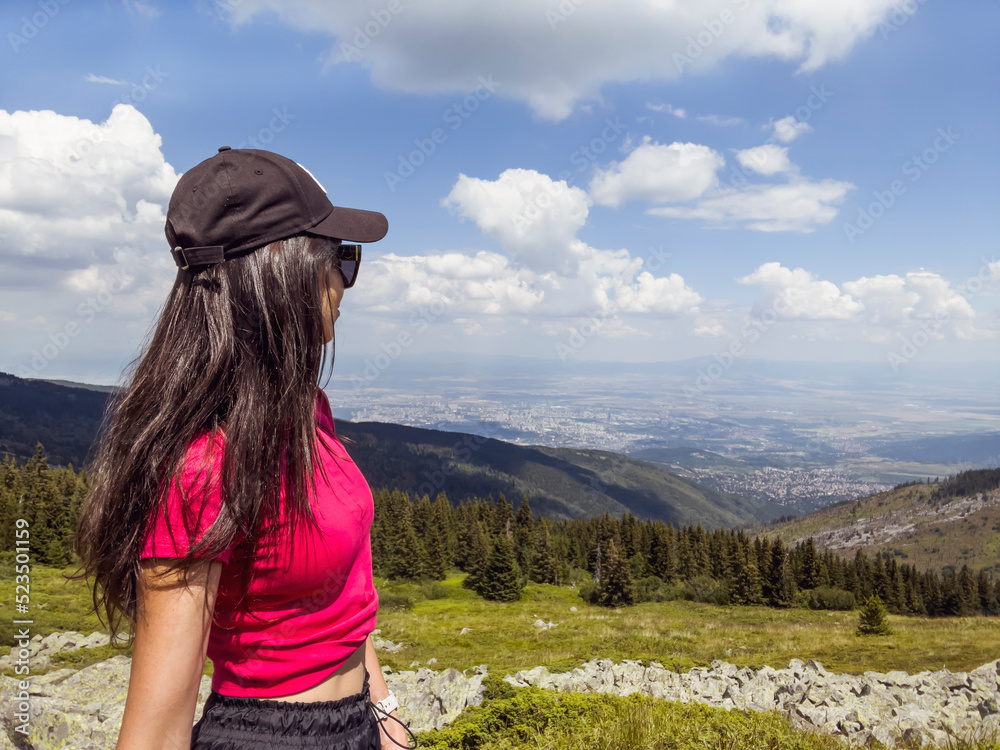 Woman with hat standing  in the summer mountain with city view . Vitosha mountain .Sofia city