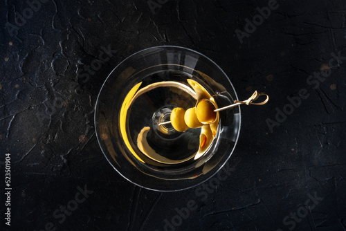 Martini, a glass with spicy olives on a toothpick, on a black background. Alcoholic cold drink, overhead shot