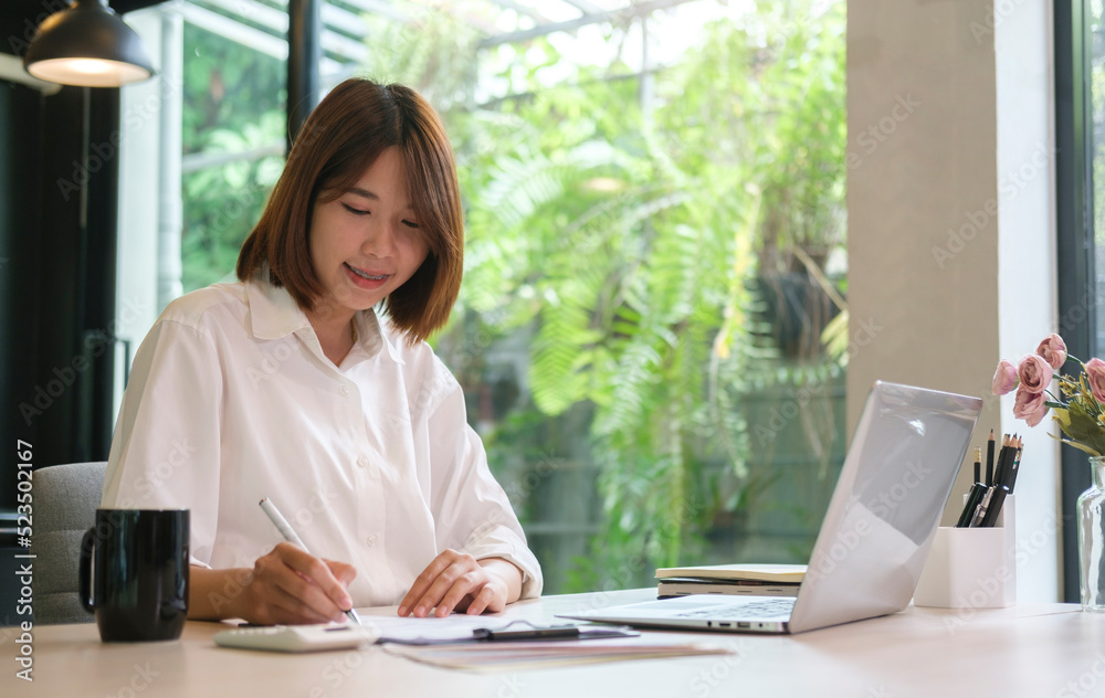 Smiling female office worker using laptop computer and making note on notebook. Smiling female office worker using laptop computer and making note on notebook.